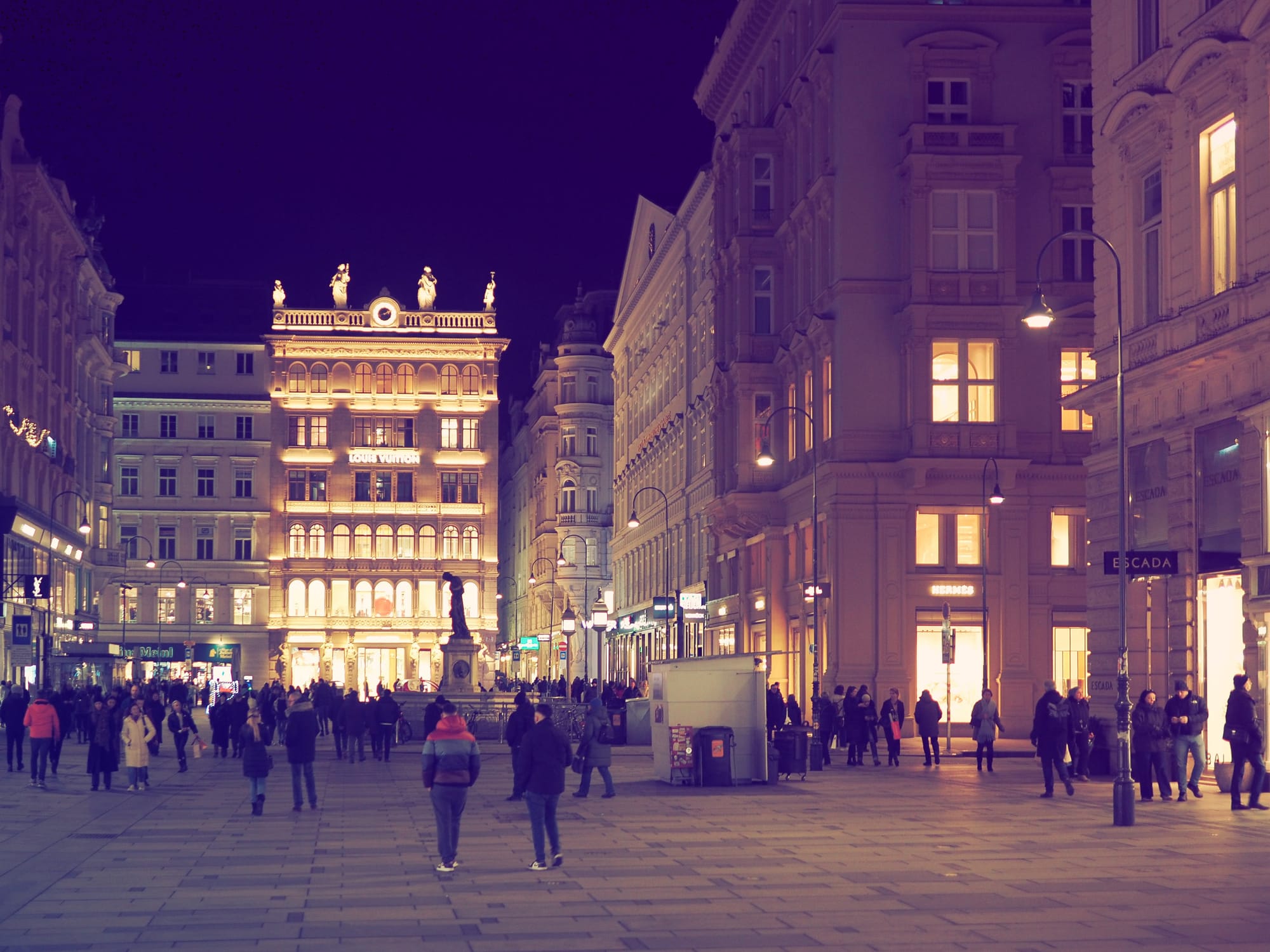 People walking across Stephansplatz at night in Vienna, surrounded by illuminated historic buildings and shopfronts.