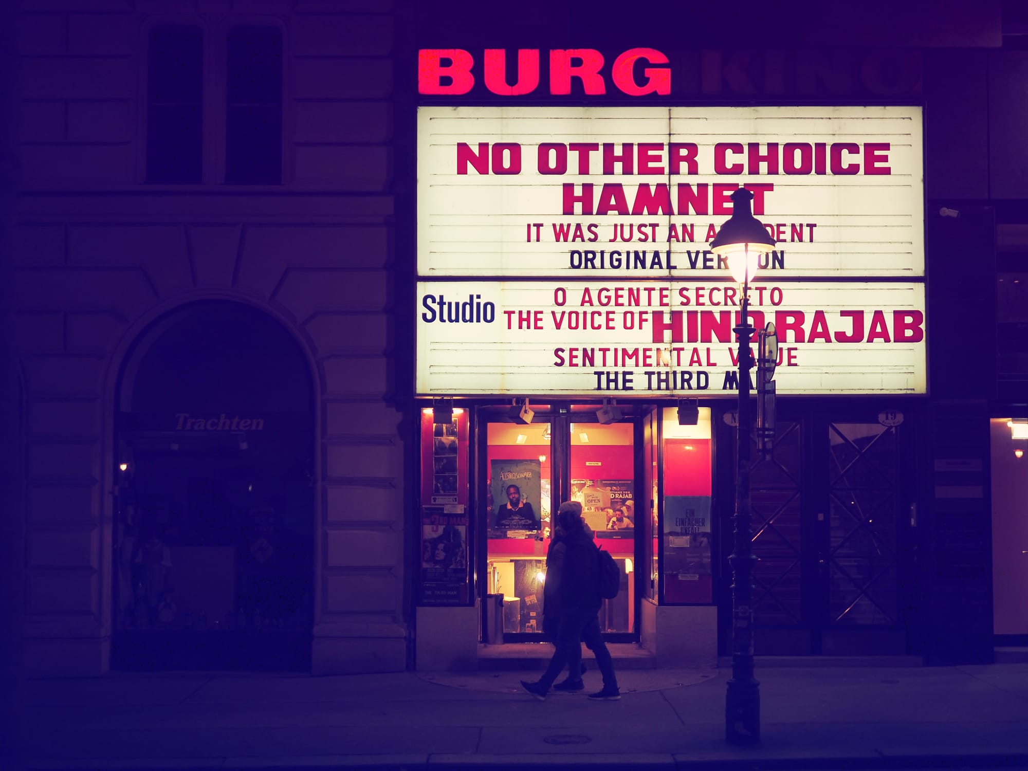 Illuminated cinema marquee at night in Vienna with a person walking past the entrance.